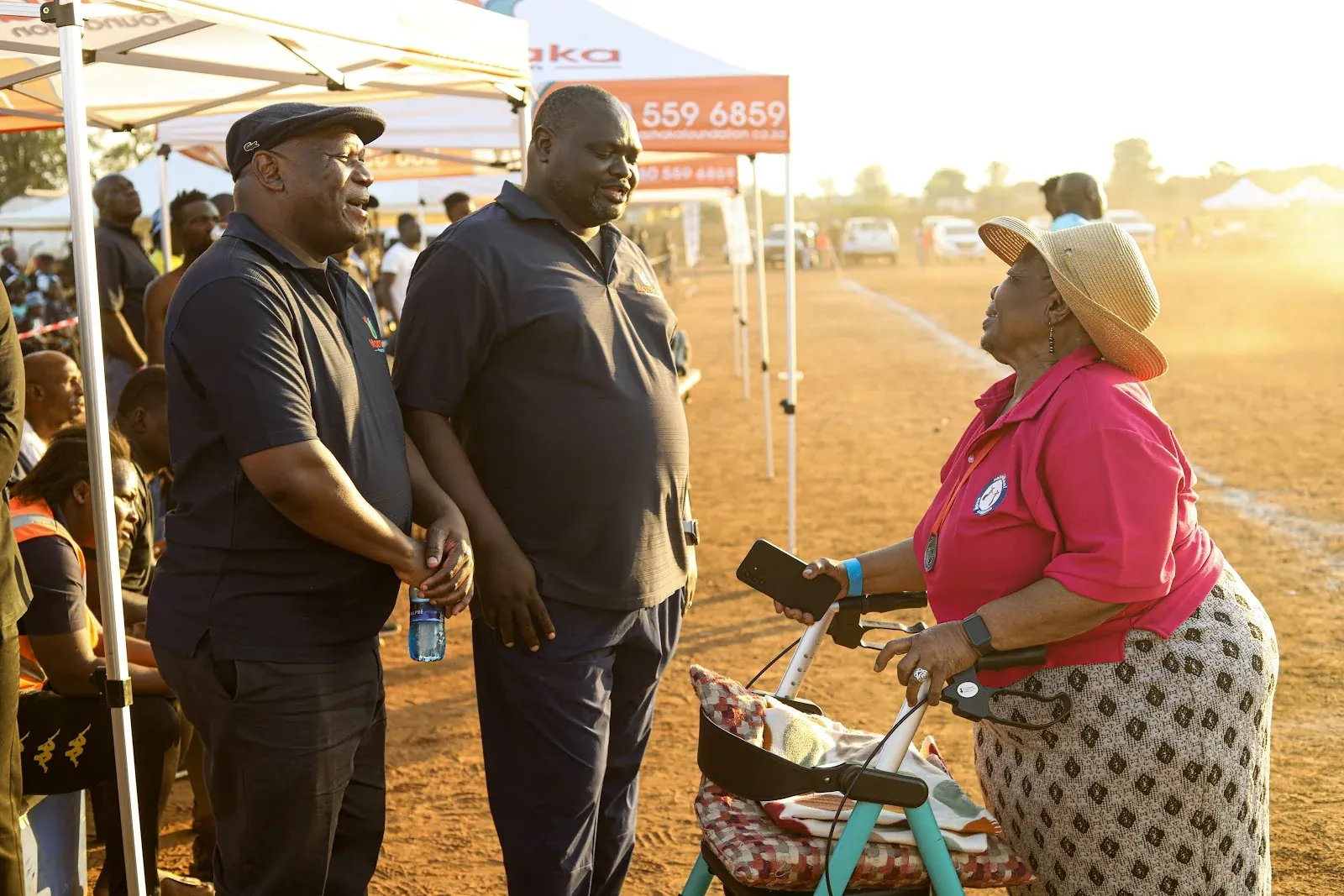 An older woman in pink speaking with community members at a Mazhaka gathering