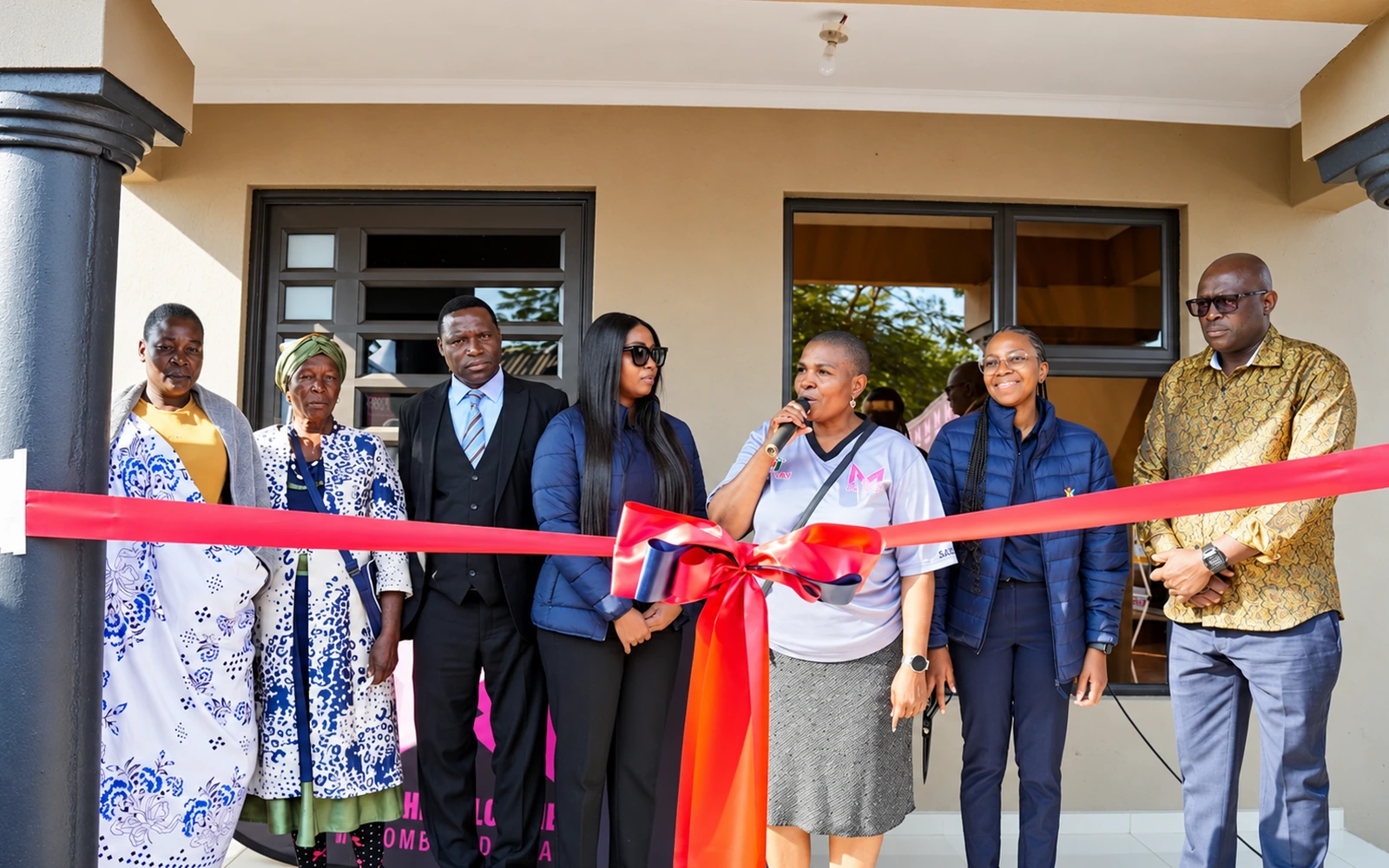 Community representatives gathered around a ribbon for a house handover ceremony