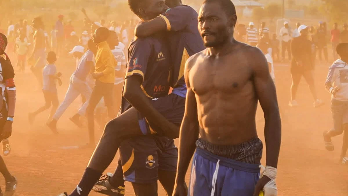 Football players celebrating together on a sunlit community pitch